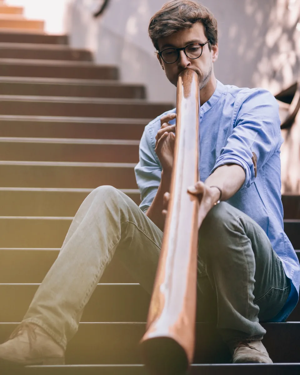 Gauthier Aubé joue du didgeridoo, assis dans un escalier